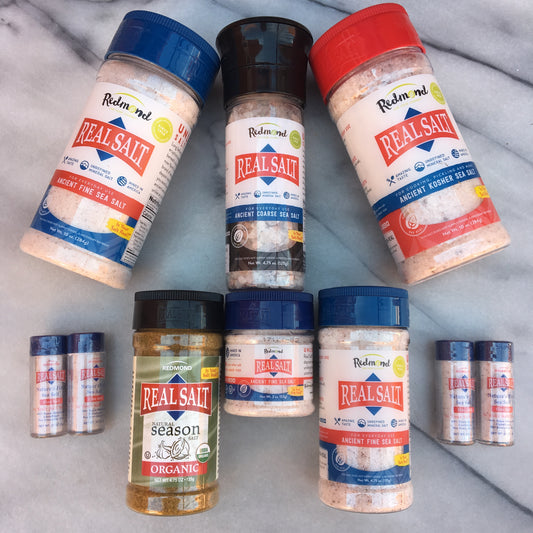 A collection of Real Salt shaker refills in various sizes displayed on a marble surface. The packaging indicates different flavors such as 'Pure', 'Season', and 'Real Salt' with the branding visible on each.